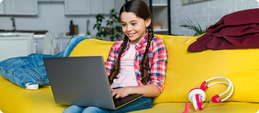 Niña sonriente usando una ordenador portátil mientras estudia