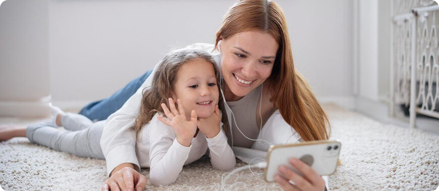 Mother and Daughter Participating in a Listening Activity with a Smartphone A mother and daughter lying on the floor, using earphones and a smartphone to engage in an English listening activity.