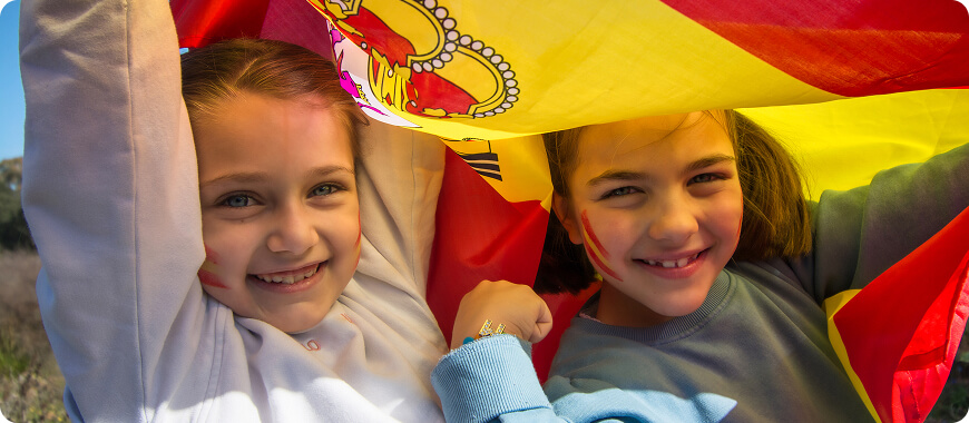 Two happy children holding the red and yellow Spanish flag.
