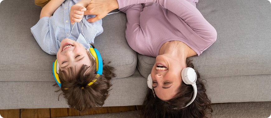 Mother and Child Improving English Listening Skills Together A mother and child lying on a couch, both wearing headphones and smiling while practicing English listening activities together.