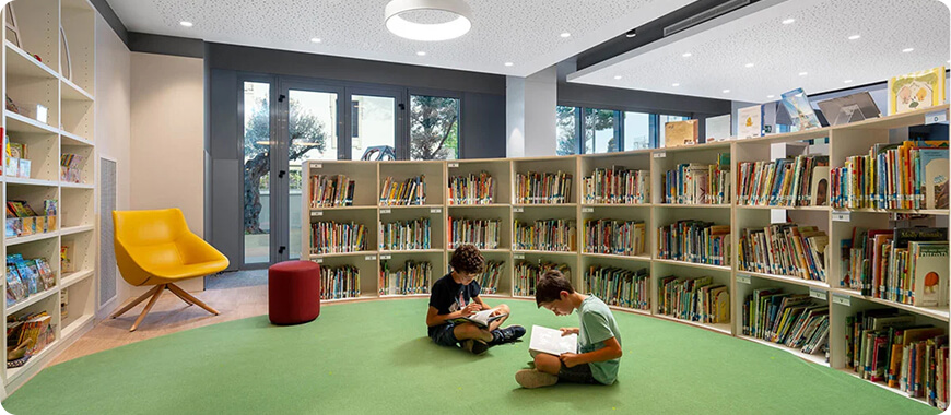 Fomento de la alfabetización y el aprendizaje en la biblioteca de la Escuela Internacional Dos niños leyendo libros en un acogedor espacio de la biblioteca con cómodos asientos