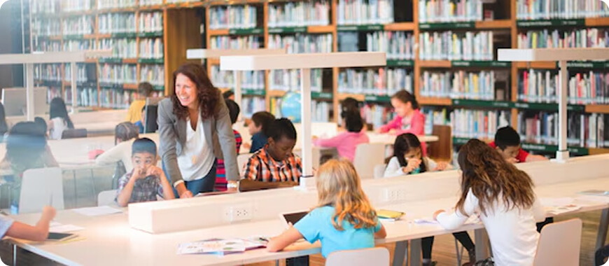 Aprendizaje interactivo en la biblioteca de un colegio internacional Profesor ayudando a los alumnos en una biblioteca bien iluminada y llena de libros y zonas de estudio